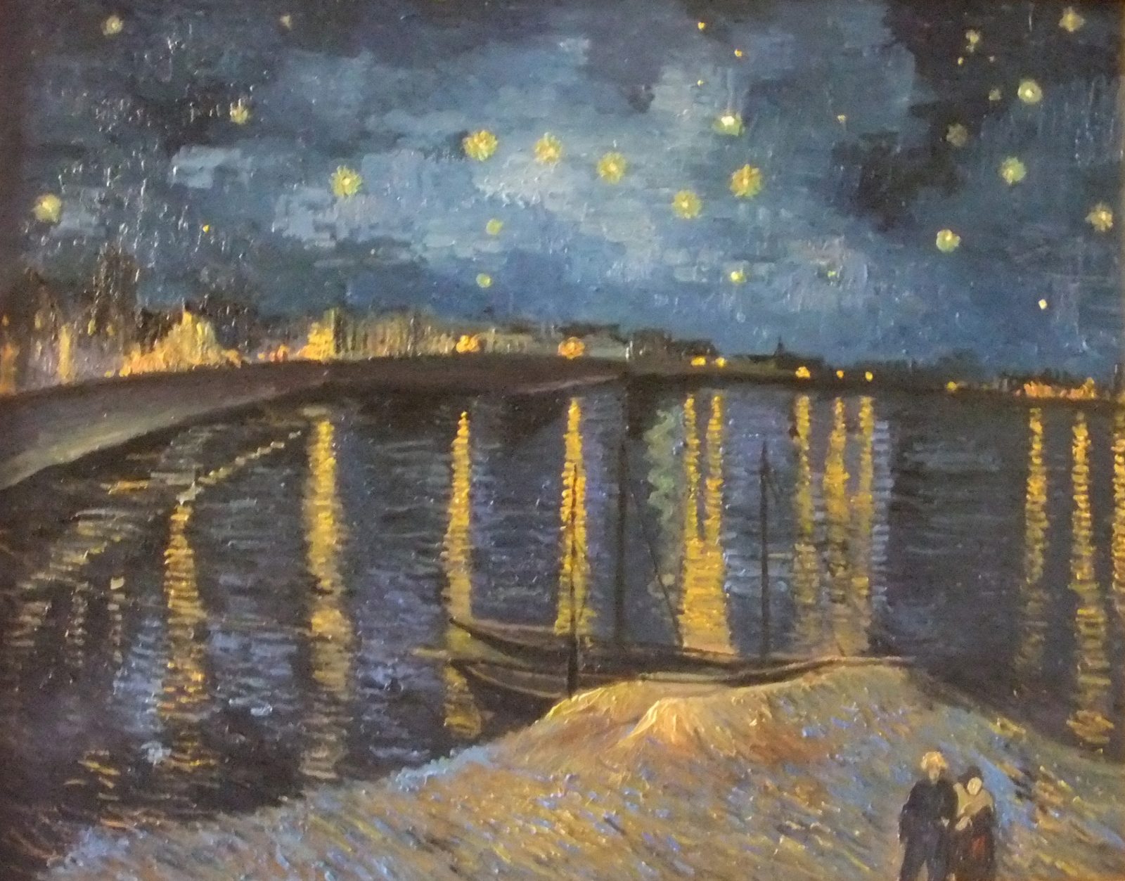 Riproduzione del dipinto Notte stellata sul Rodano di Vincent Van Gogh, che mostra un cielo notturno blu intenso con stelle luminose e un fiume Rodano scuro riflettente, illuminato da luci artificiali sulla riva e da una coppia passeggiante.